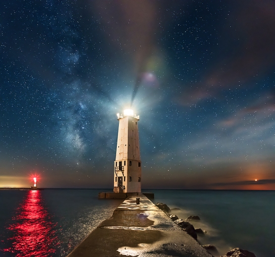 Photo: The lighthouse in Frankfort Michigan lights up a hazy sky under a sky full of glittering stars, the Milky Way, and a setting moon.