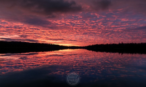 A dramatic red sunrise reflects in perfectly still waters