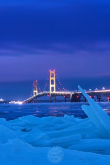 Shards of ice frame a golden Mackinac Bridge on a blue January night